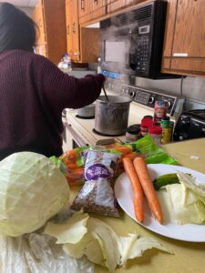 An image of ingredients for cooking, with someone preparing food in the background.