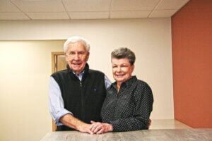 George Winn and his wife posing for a photo against a white wall, holding hands