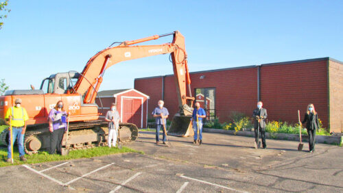 Image of a construction equipment outside Holy Trinity Lutheran Church with individuals spaced out, wearing face mask and hard hats.